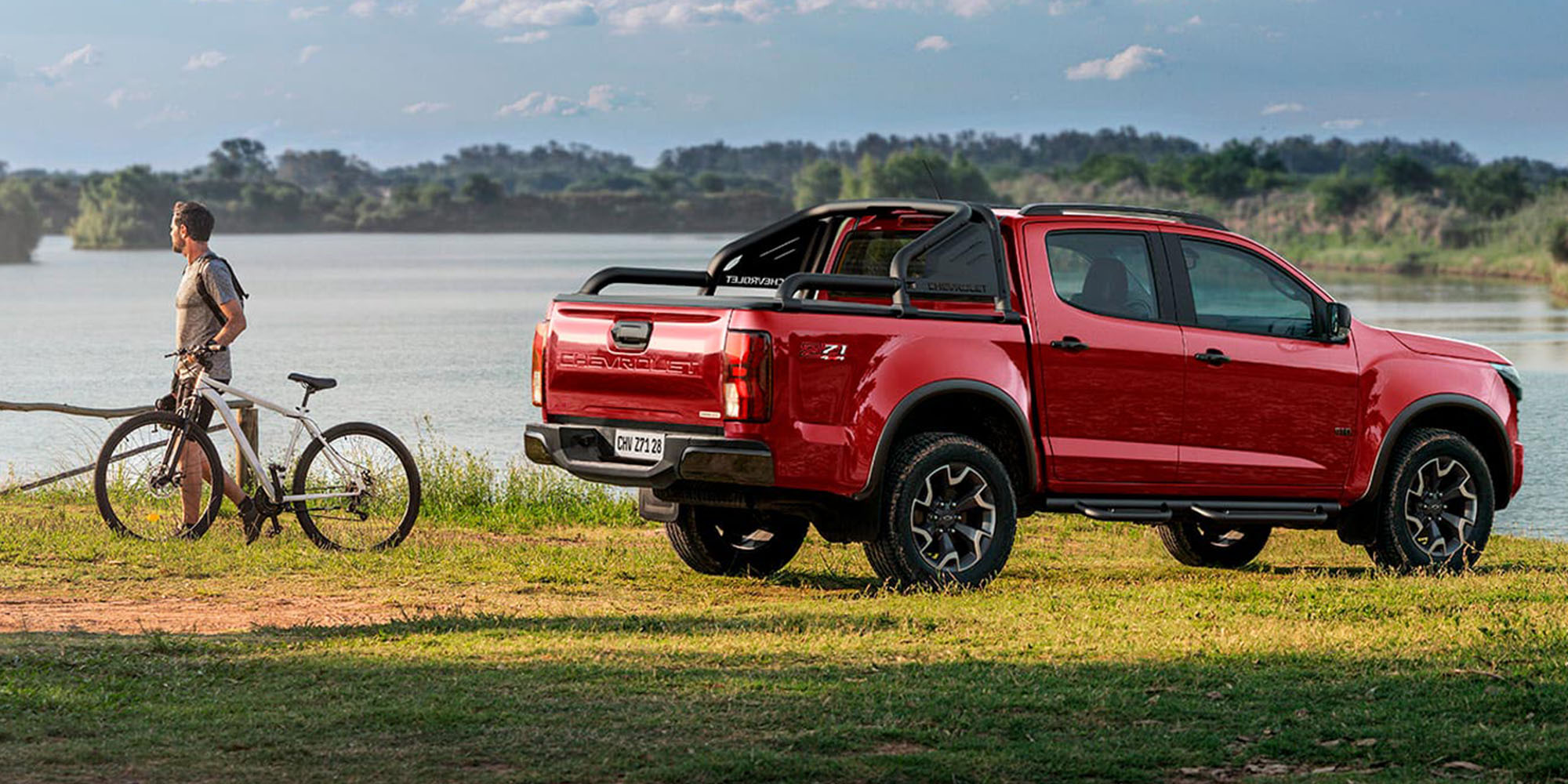 Chevrolet Colorado roja parqueada sobre pasto junto a un lago resaltando su diseño pickup